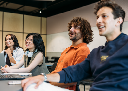 four people smiling and laughing, sitting at a desk.