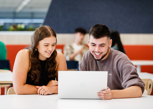 Two students looking at a laptop, smiling and choosing their course preferences
