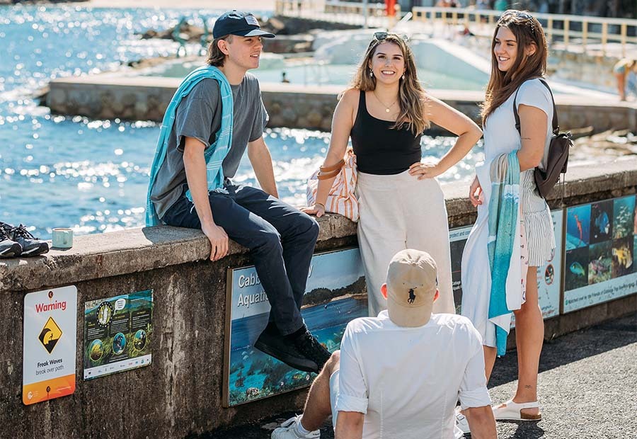 Students sitting on a wall at the edge of the beach