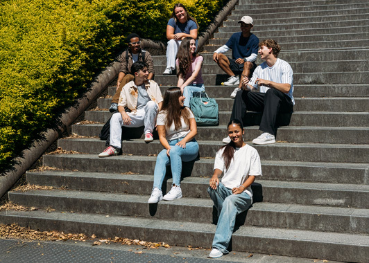 Group of uni students sitting on outdoor campus steps and chatting, laughing and smiling