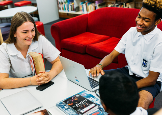 Three high school students working and talking while sitting around a table in a school library