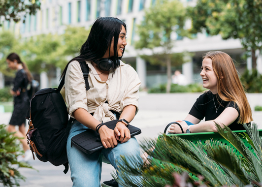 Two smiling female students talk to each other on campus